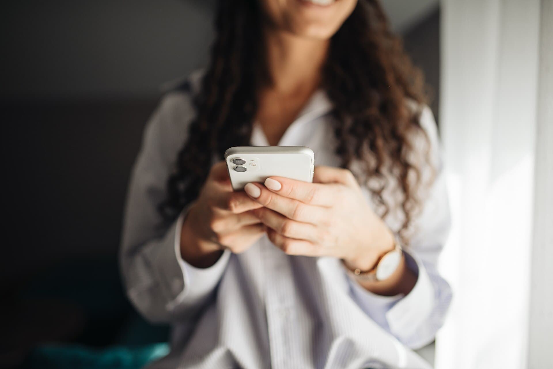 A smiling woman holding a phone in soft morning light